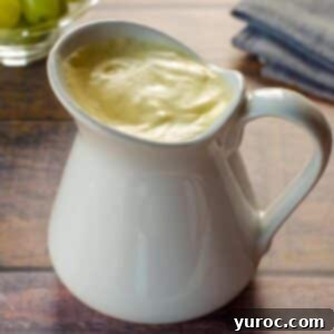 Lighter Hollandaise 9 Healthy Hollandaise sauce in a large white creamer, with a bowl of green grapes in background and grey linen