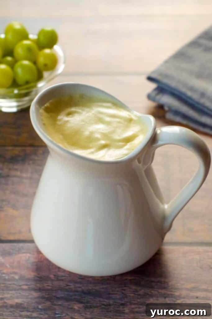 Lighter Hollandaise 7 Healthy Hollandaise sauce in a large white creamer, with a bowl of green grapes in background and grey linen