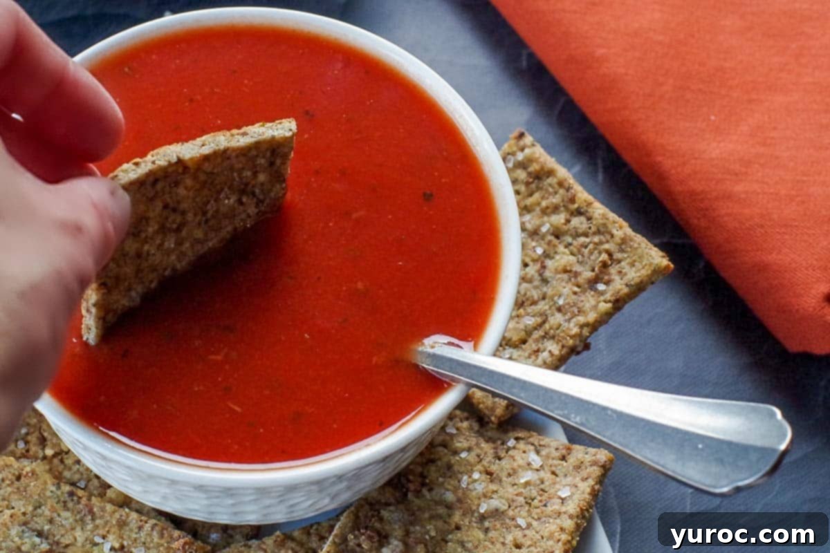 Golden Stuffing Crisps 5 A crispy leftover stuffing cracker being dipped into a bowl of vibrant tomato soup, highlighting a perfect pairing.