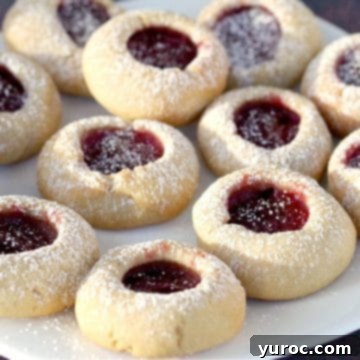 Golden-brown raspberry jam thumbprint cookies elegantly arranged on a clean white plate.