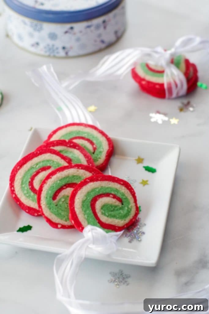4 Christmas pinwheel cookies on a white plate with 3 cookies in a ribbon in the background, as well as a cookie tin