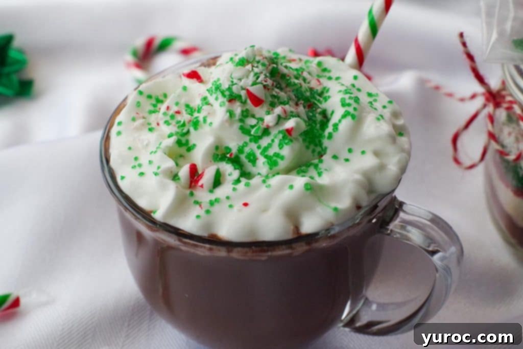 candy cane hot chocolate in a clear mug with whipped cream, green sprinkles and crushed candy canes