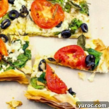 A vibrant Greek Filo Pizza, freshly baked and sliced, presented beautifully on a clean white surface.