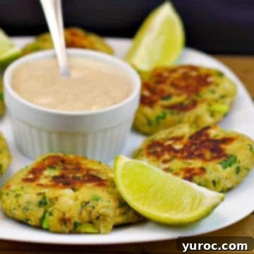 Delicious canned salmon patties arranged on a white plate, with a small bowl of dip in the center and fresh lime wedges for garnish.
