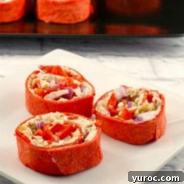 Chicken tortilla pinwheels arranged on a pristine white plate, with a larger tray of pinwheels blurred in the background.