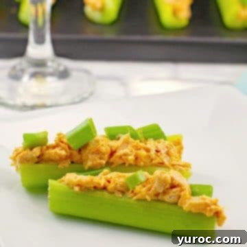 Two enticing buffalo chicken celery sticks presented on a white plate, with a glass of wine and a black platter holding more celery sticks in the background.