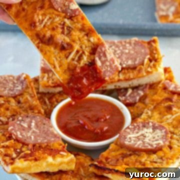 A pizza dipper being plunged into a rich pizza sauce, with several other dippers arranged around it on a white plate, alongside a separate portion of white ranch dip.