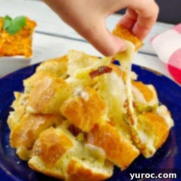 A hand gently pulling a piece of cheesy pull-apart bread from its bun, showcasing its enticing texture.