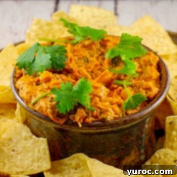 Hearty artichoke pizza dip served in a rustic brown ceramic container, surrounded by a generous scattering of crisp nachos, inviting you to dig in.