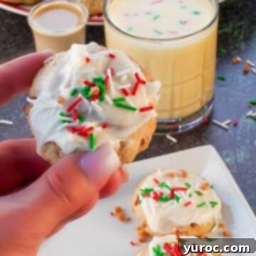 A delightful eggnog and Baileys Irish Cream cookie, held aloft, with a pristine white plate showcasing more cookies in the background.