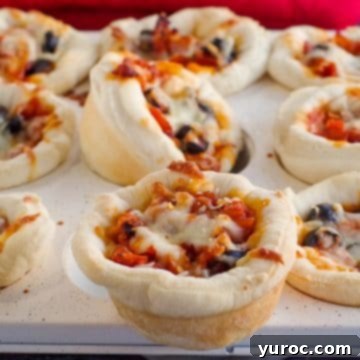 A muffin tin generously filled with pizza cupcakes, with one perfectly baked pizza cupcake prominently displayed on top in the foreground.