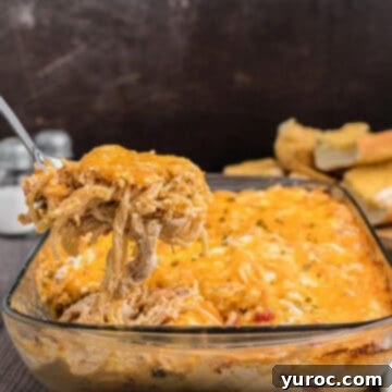 chicken spaghetti in a glass casserole dish with spoon holding up portion of it over the dish