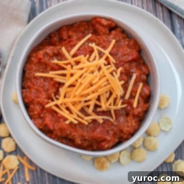 11 Legendary Chili Recipes 5 tailgate chili in a white bowl on a platter, with cheese on top and little crackers scattered around