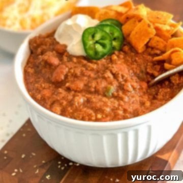 11 Legendary Chili Recipes 6 chili in a white casserole bowl, topped with jalapenos, sour cream and chips, on a brown cutting board