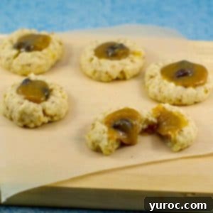 Butter Tart Thumbprint Delights 5 butter tart cookies on a piece of parchment paper (on cutting board) with 1 cookie split in half