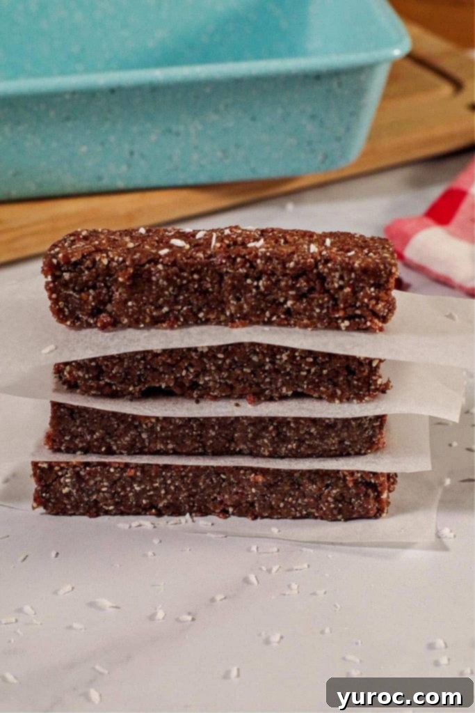 4 No bake energy bars stacked with parchment paper between them and blue loaf pan on cutting board in background