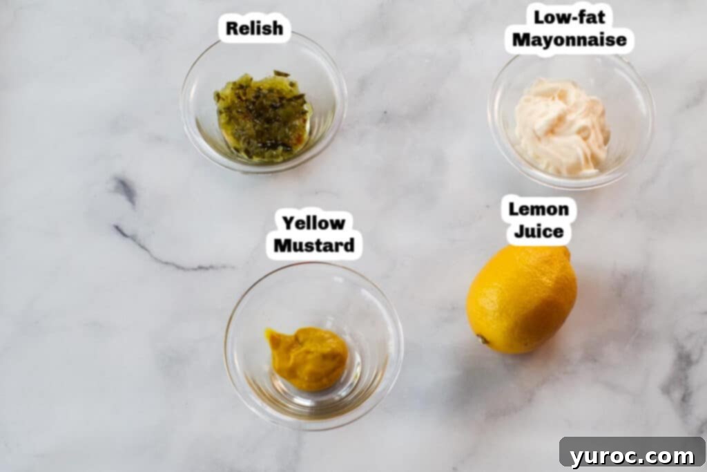 A selection of fresh ingredients for healthy tartar sauce laid out on a clean kitchen countertop, including lemons, mustard, relish, and a jar of mayonnaise.