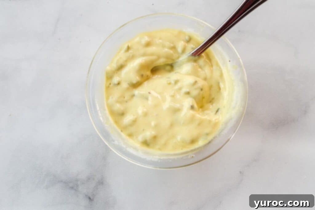 Healthy tartar sauce gently stirred in a clear glass bowl, showcasing its smooth texture and readiness for serving, on a kitchen counter.