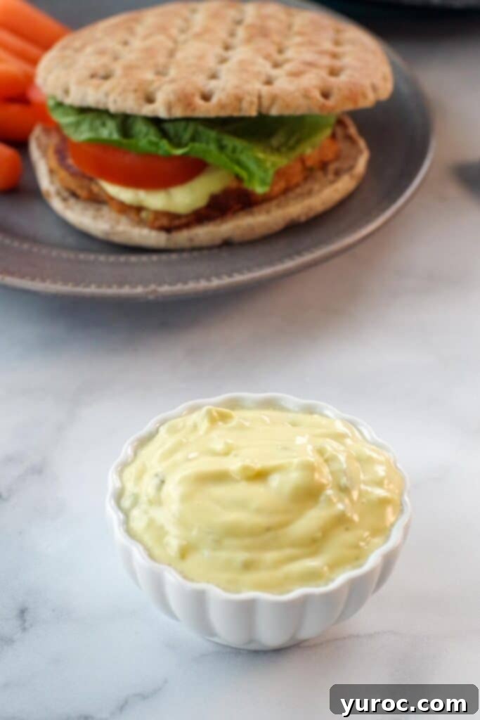 A small white dish of tartar sauce placed in the foreground, with a perfectly grilled tuna burger blurred in the background, illustrating a serving suggestion.
