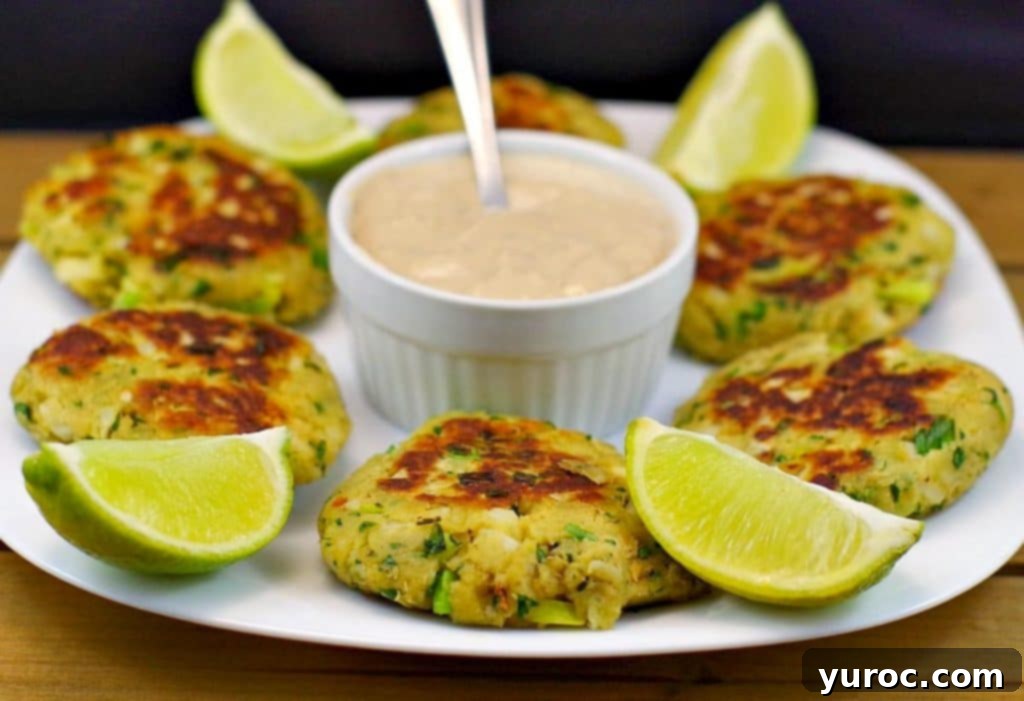 Beautifully pan-fried salmon patties arranged on a white plate with a central dish of tartar sauce and fresh lime wedges, ready for an elegant meal.