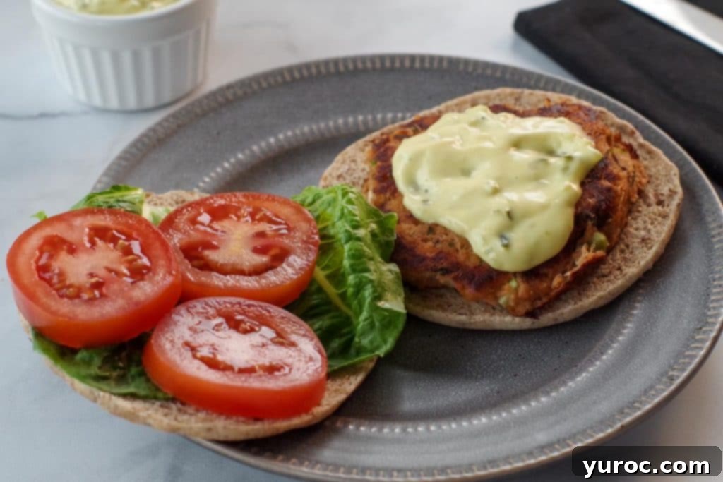 Tuna patty on a bun with tartar sauce on one side and tomatoes and lettuce on the other side