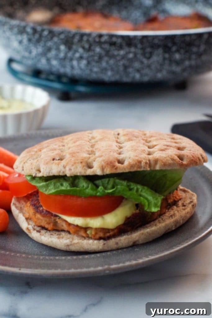 tuna burger on grey plate with frying pan with tuna patties in the background