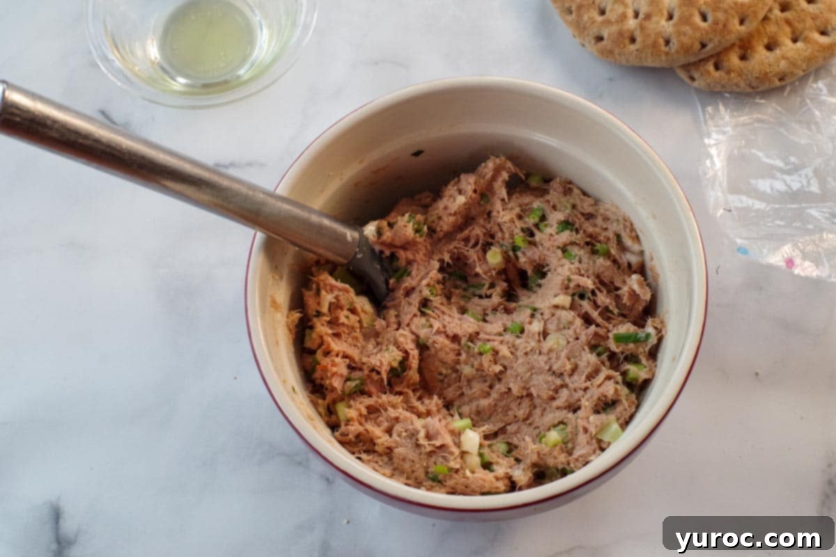 tuna burger ingredients mixed together in a bowl with a spoon and olive oil in the background