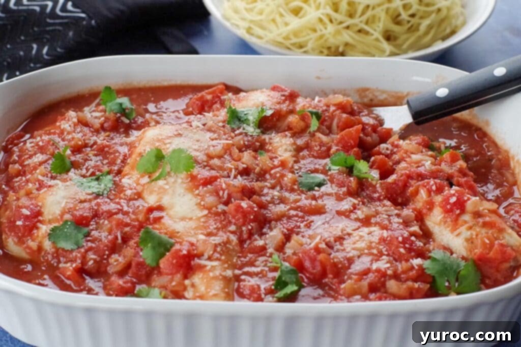 Rustic Baked Chicken Cacciatore 1 Baked chicken cacciatore in a white casserole dish, ready to serve, with a black serving utensil and a bowl of pasta noodles in the background.