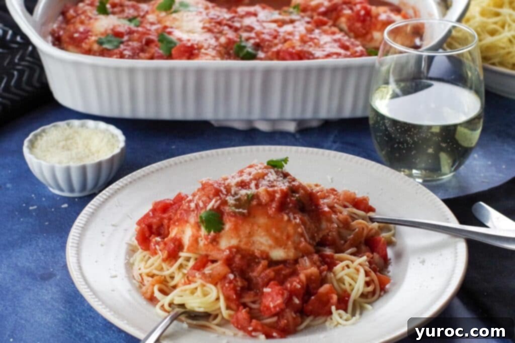 Rustic Baked Chicken Cacciatore 3 Plated chicken cacciatore served over noodles on a white plate, garnished with fresh herbs, with a glass of white wine and a casserole dish of more chicken cacciatore in the background.