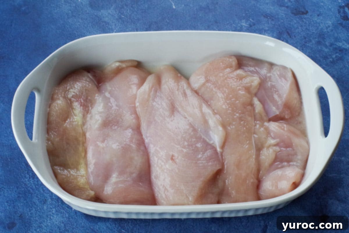Rustic Baked Chicken Cacciatore 4 Raw boneless, skinless chicken breasts laid flat in a white casserole dish, ready for sauce.