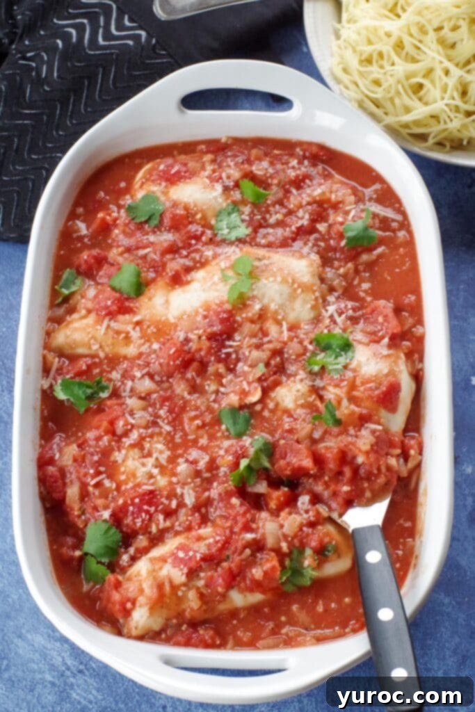 Rustic Baked Chicken Cacciatore 8 A top-down view of baked chicken cacciatore in a white casserole dish, garnished with fresh herbs, with a serving utensil and a side of pasta in the background.