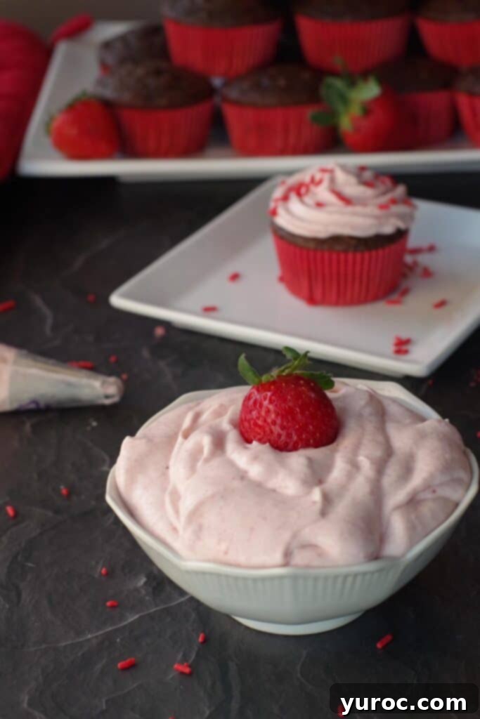 strawberry frosting in white bowl with cupcake on a plate in the background
