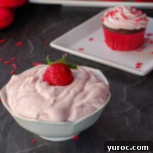 strawberry frosting in white bowl with cupcake on a plate in the background