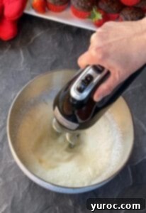 whipping cream and powdered sugar in a mixing bowl, being whipped with electric hand mixer