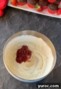jam, vanilla extract and piping gel added to whipped cream powdered sugar mixture in bowl