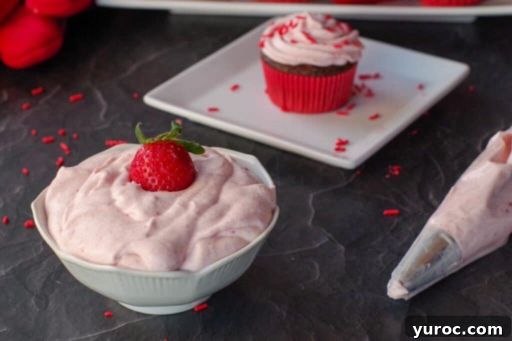 strawberry frosting in white bowl with cupcake on a plate in the background