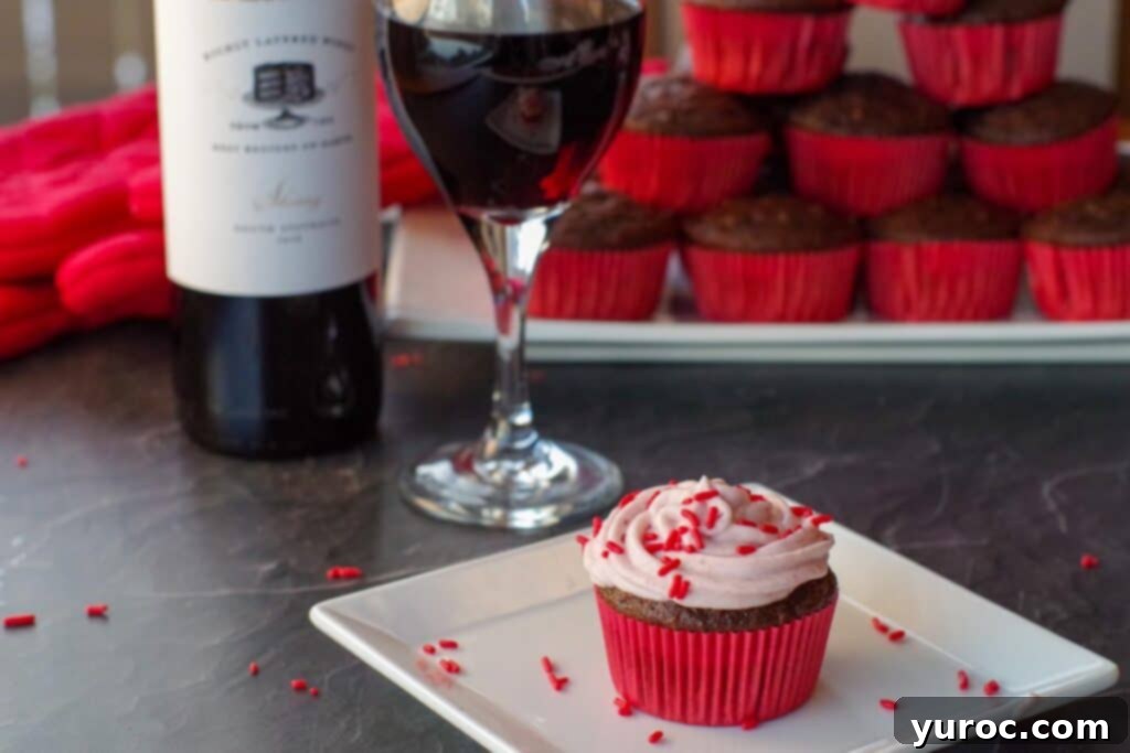 Effortless Elegance Red Wine Chocolate Cupcakes 7 A stunning shot of a red wine cupcake on a white plate, with a wine bottle, glass, and additional cupcakes softly blurred in the background.