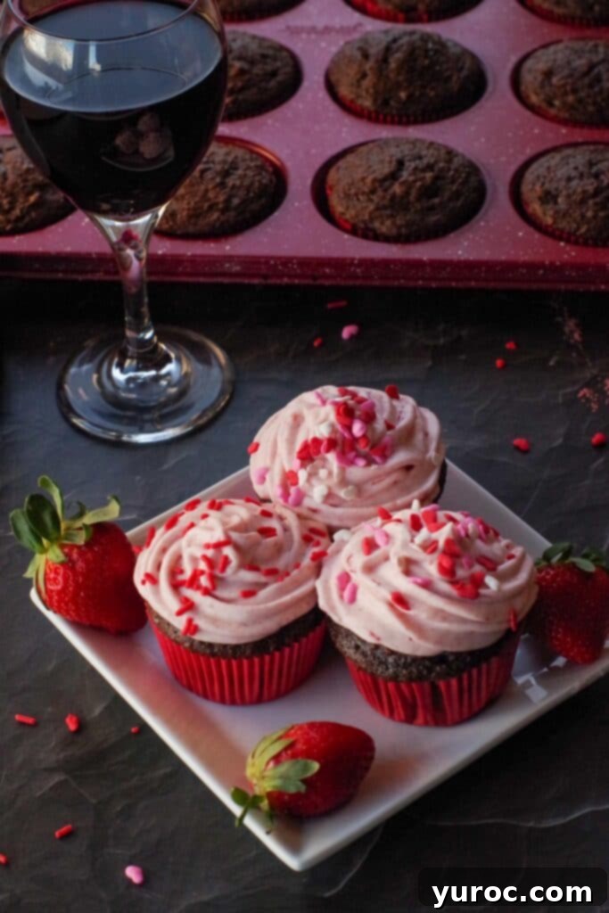 Effortless Elegance Red Wine Chocolate Cupcakes 8 Three perfectly frosted red wine cupcakes on a white plate, artfully arranged with a glass of red wine and a muffin tin in the background.