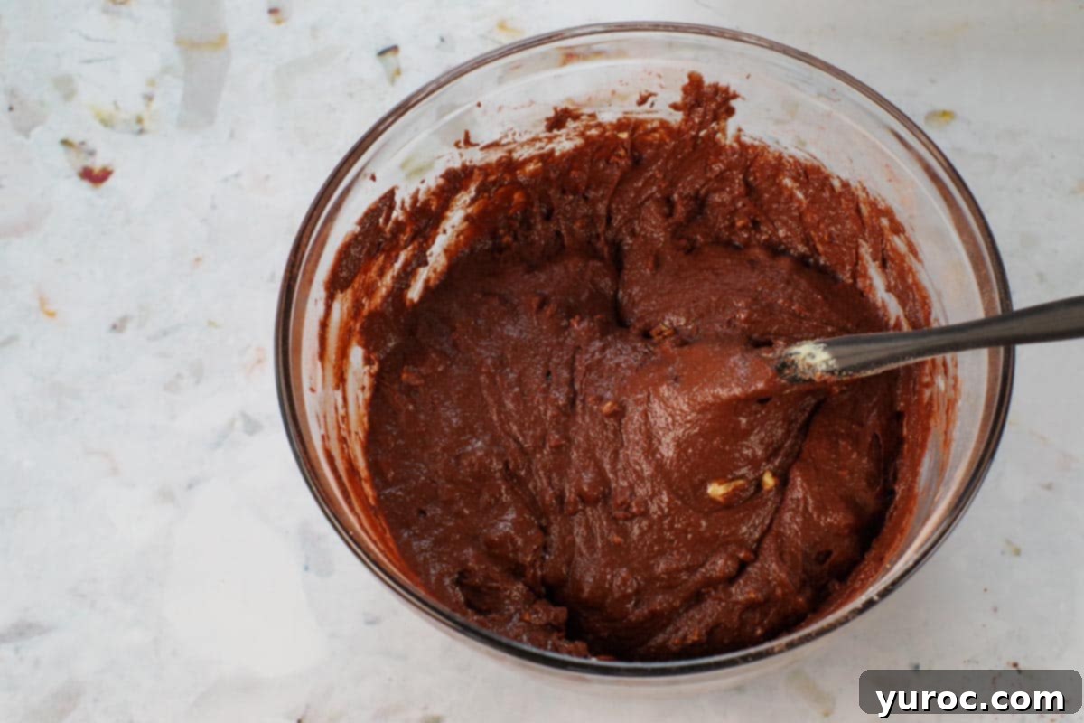Blender Bliss Chocolate Zucchini Bread 10 Chopped pecans sprinkled into the smooth chocolate zucchini bread batter in a glass bowl, with a black spatula nearby, indicating the final addition before baking.