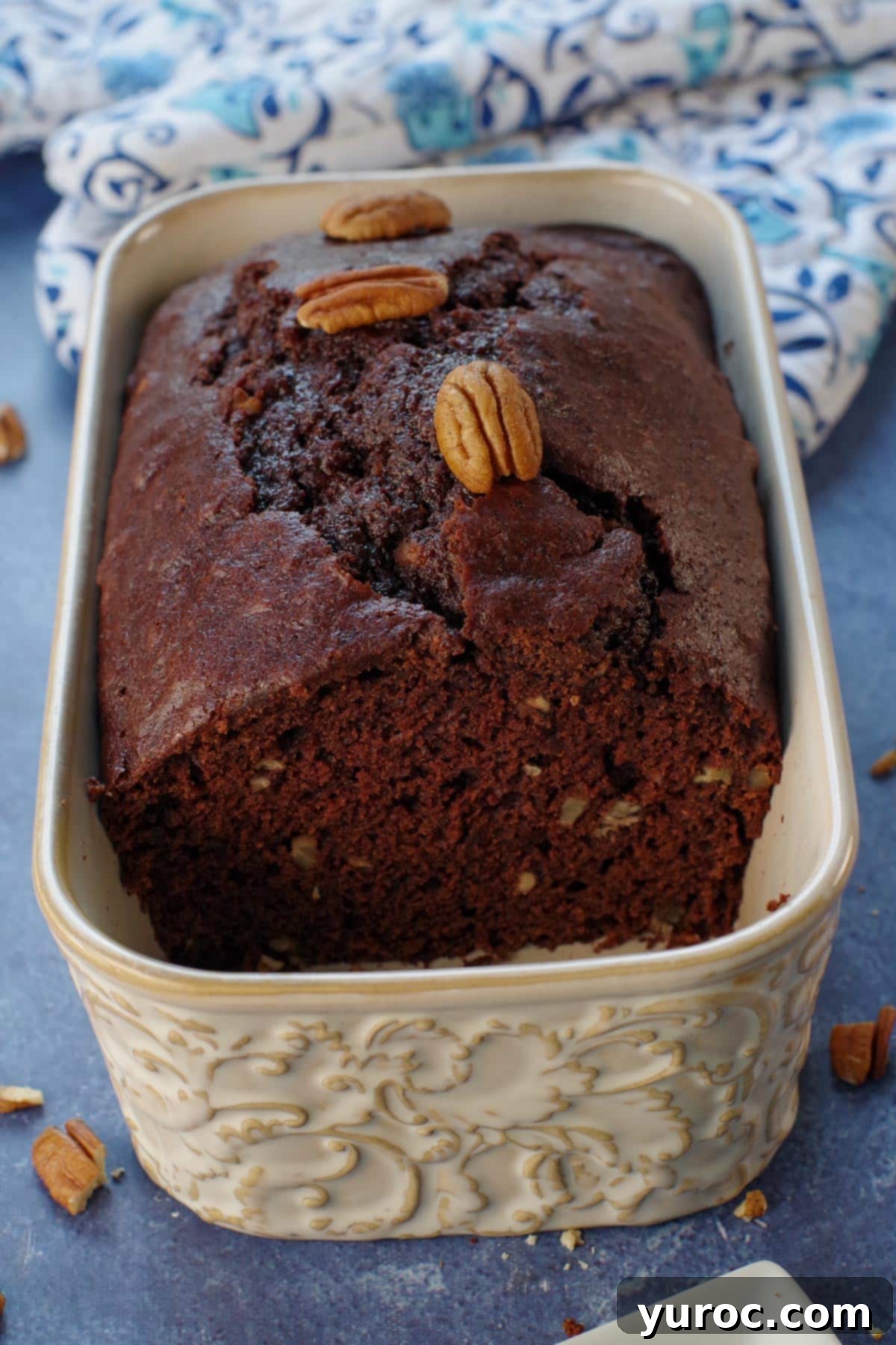 Blender Bliss Chocolate Zucchini Bread 13 A freshly baked Chocolate Blender Zucchini Bread loaf on a white surface, with several slices already cut, revealing its moist, rich interior speckled with pecans.