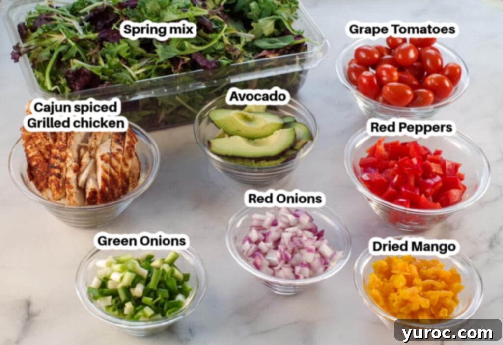 Fiery Cajun Mango Chicken Salad 3 photo with ingredients for Cajun chicken avocado mango salad (labelled) in glass bowls with container of spring mix in the back