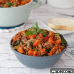 Lentil and sausage stew in blue bowl on white surface with light blue pot of stew in the background
