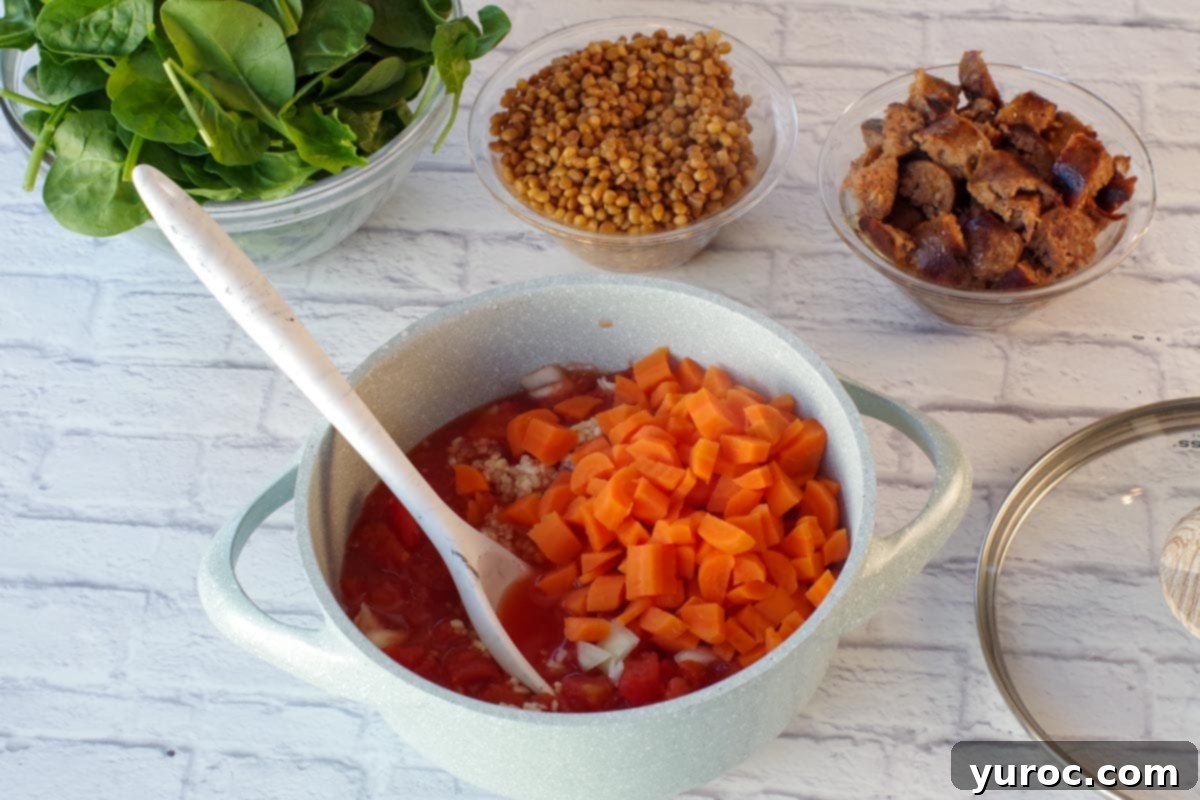 carrots, tomatoes and onions in pot with lentils, spinach and cooked sausage in background