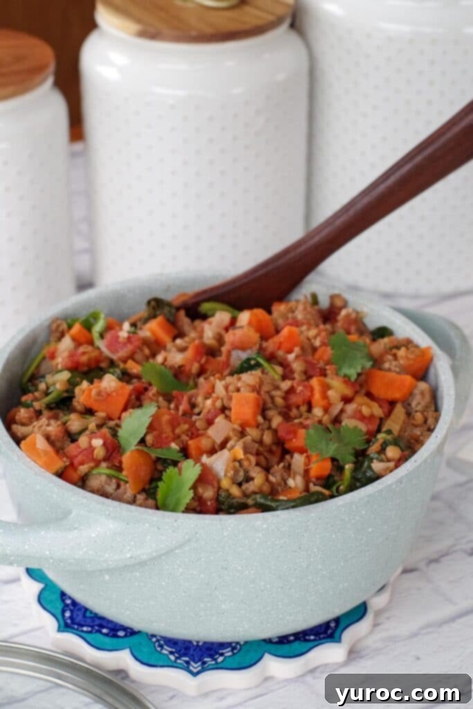 Lentil Sausage Stew with spinach in a light blue pot with white canisters in the background