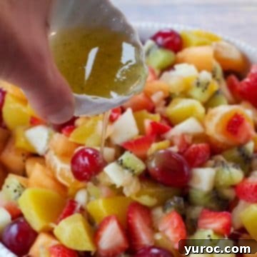 A vibrant, easy fruit salad presented in a white bowl, with a luscious honey lime dressing being poured gracefully over the colorful mix.