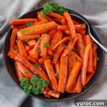 Perfectly roasted brown sugar glazed carrots served in a sleek black bowl, accompanied by a spoon, all resting on elegant grey linen.