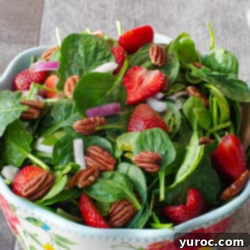 A refreshing strawberry spinach pecan salad beautifully presented in a large bowl with a delicate flower print, accompanied by elegant wooden serving utensils.