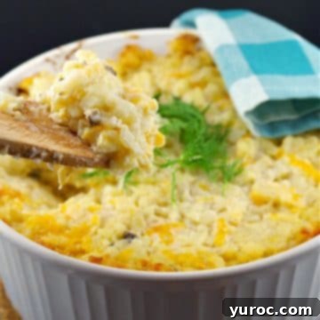 A bubbling white casserole bowl filled with Potatoes Romanoff, with a wooden spoon holding up a spoonful to showcase its creamy texture.
