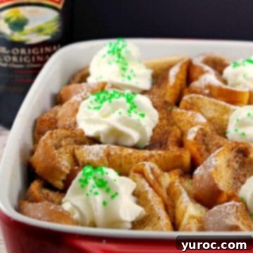 Baileys French Toast Casserole in a white and orange baking dish, with a bottle of Baileys Irish Cream in the soft-focus background.