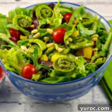 A refreshing fiddlehead spring salad elegantly presented in a blue bowl, resting on a clean white surface.